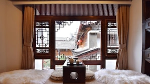 A traditional room with a view through a wooden lattice window, a small table with a teapot, and two fluffy cushions on a low bed.