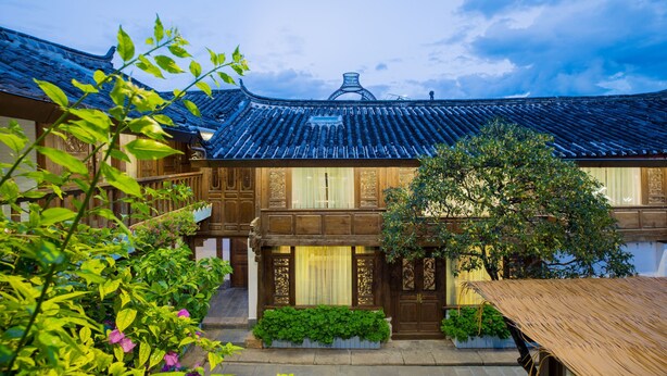 A traditional wooden building with a tiled roof, surrounded by greenery and a wooden table.