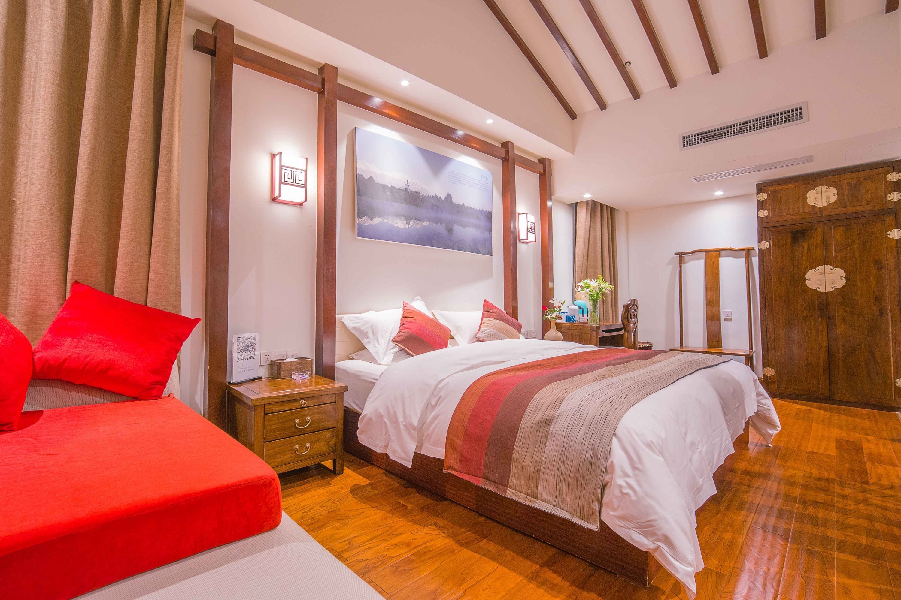 Quarto de hotel com cama grande, mesa de cabeceira, criado-mudo e guarda-roupa de madeira.
