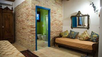Una habitación con pared de ladrillo, armario de madera, sofá con cojines estampados, espejo y suelo de baldosas.