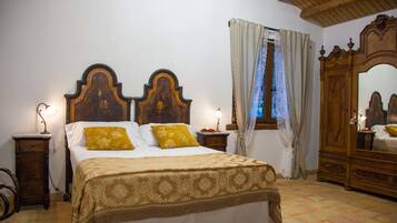 A bedroom with a large bed, wooden headboard, two bedside tables with lamps, a wardrobe, and a window with curtains.