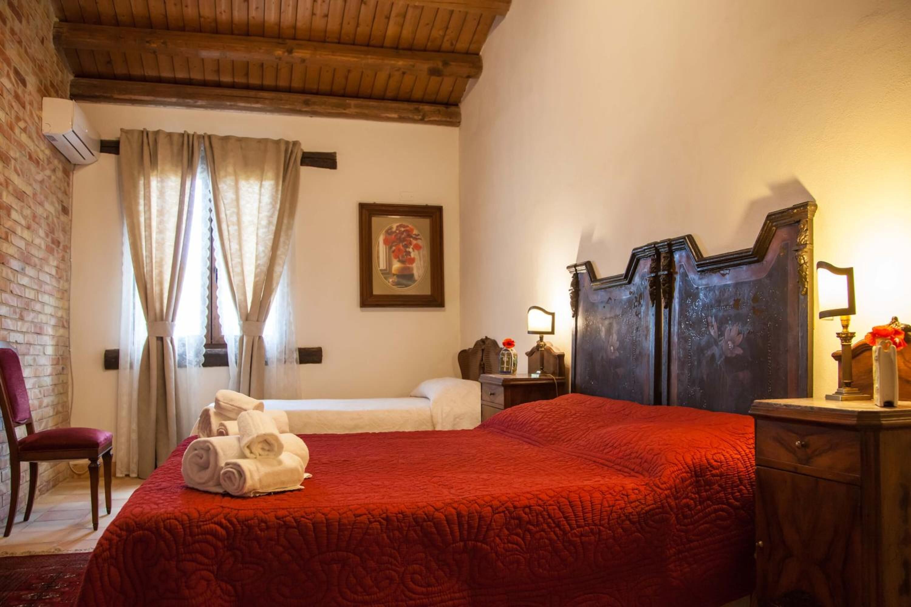 Quarto de hotel com uma cama grande, uma cama menor, cabeceira de madeira, mesa de cabeceira, uma cadeira e um quadro na parede.