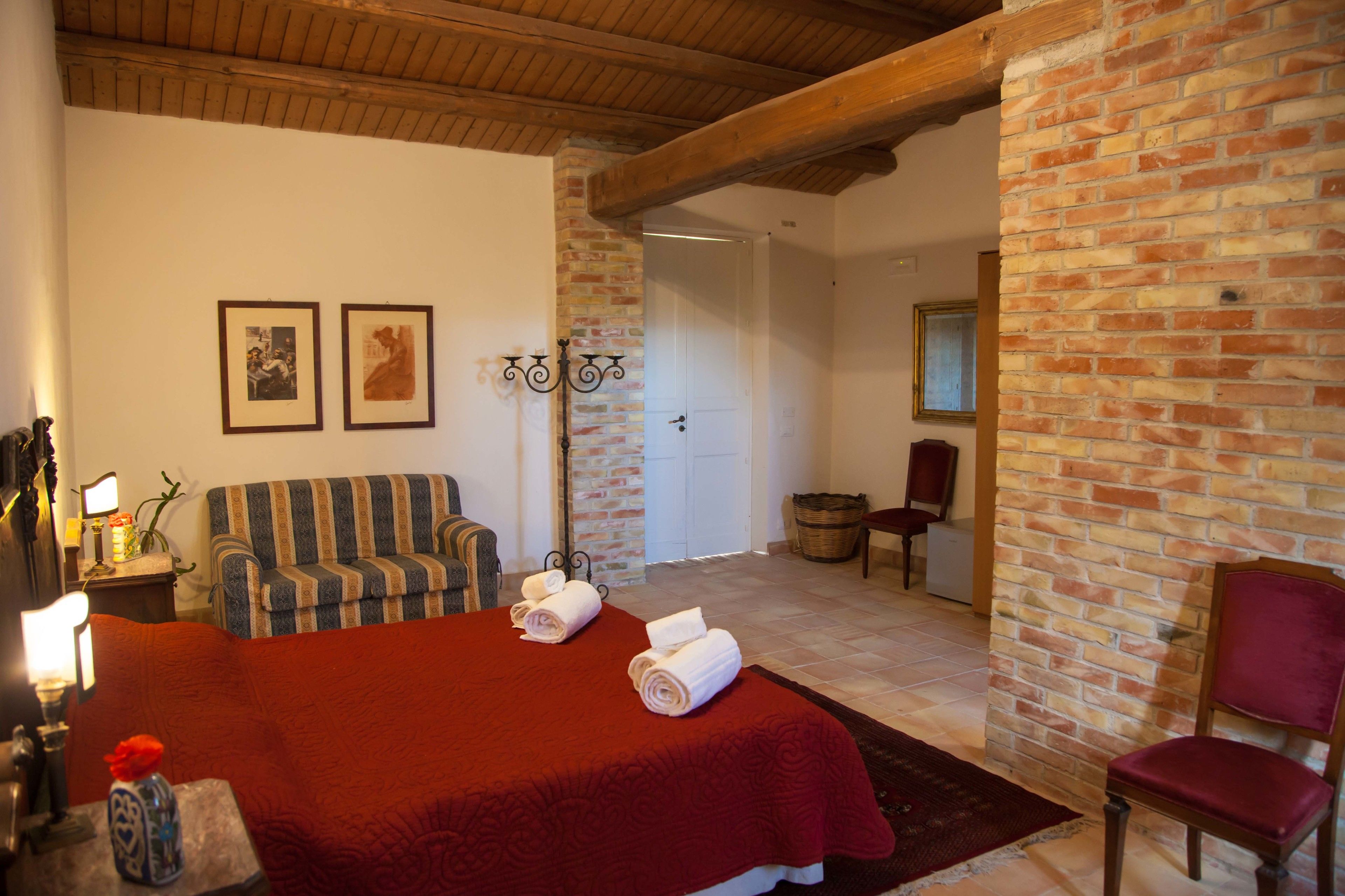 Habitació d'hotel amb un llit gran, un sofà amb ratlles, una paret de maó i un sostre de fusta.