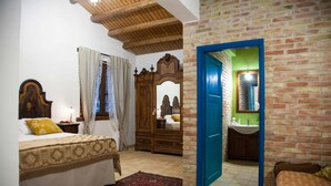Een slaapkamer met een bed, een houten garderobe, een spiegel en een badkamer met een wastafel en spiegel.