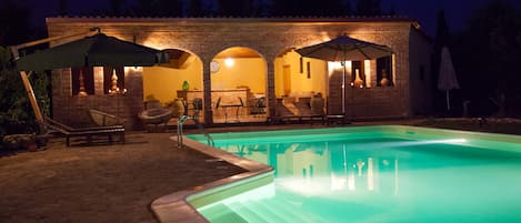 A brick building with a swimming pool, outdoor seating, and umbrellas.