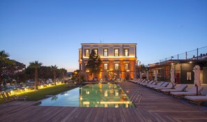 A hotel with a swimming pool, lounge chairs, and a well-lit facade. - Cunda Callisto Despot Evi +12 (Ayvalik)