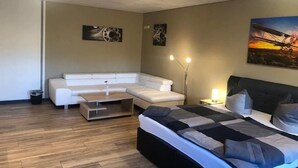 A modern bedroom with a large bed, a white sofa, and a small coffee table. There are two wall-mounted lamps and a painting on the wall. - Pension Flying Ranch (Koelleda)