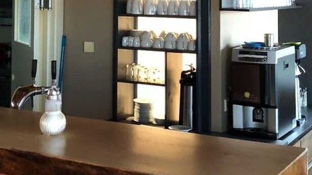 A coffee shop interior with a counter, espresso machine, shelves with cups, and hanging lights. - Pension Flying Ranch (Koelleda)