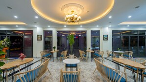 A modern interior with round tables and chairs, a central chandelier, and large windows. - Sofia Hotel (Phu Quoc)