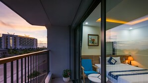 A hotel room with a balcony, a bed, a chair, a table, and a potted plant. - Sofia Hotel (Phu Quoc)