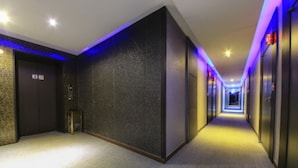 Een hotelhal met vloerbedekking, een gestructureerde wand aan één kant en deuren aan weerszijden.