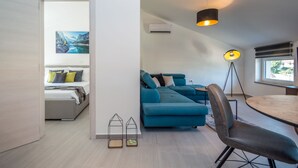 Een moderne woonkamer met een blauwe bank, een eettafel en een vloerlamp.