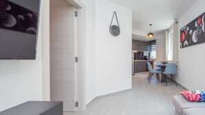 Een moderne woonkamer met een bank, een salontafel en een eethoek met stoelen en een tafel. Achtergrond is een keuken met een hanglamp.
