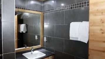 A bathroom with a wooden ceiling, dark tiled walls, a mirror with a wooden frame, a sink, and a toilet.