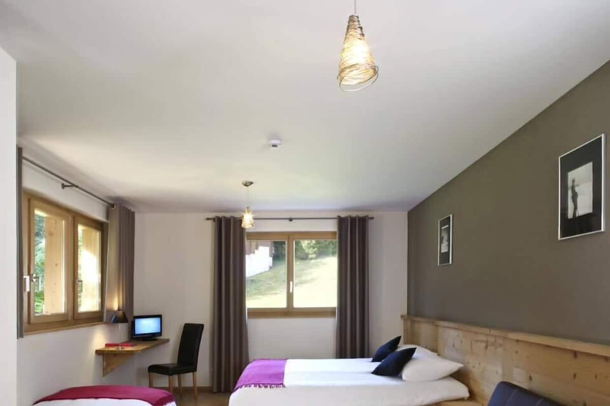 Ein Zimmer mit zwei Betten, einem Schreibtisch mit Computer, einer Couch und einer Pendelleuchte.