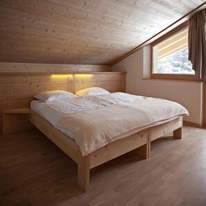 Un dormitorio de madera con cama, mesitas de noche y ventana con vistas a la nieve.