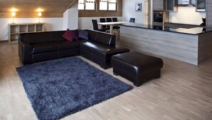 A spacious living area with a large black leather sofa, a blue rug, and a wooden ceiling.