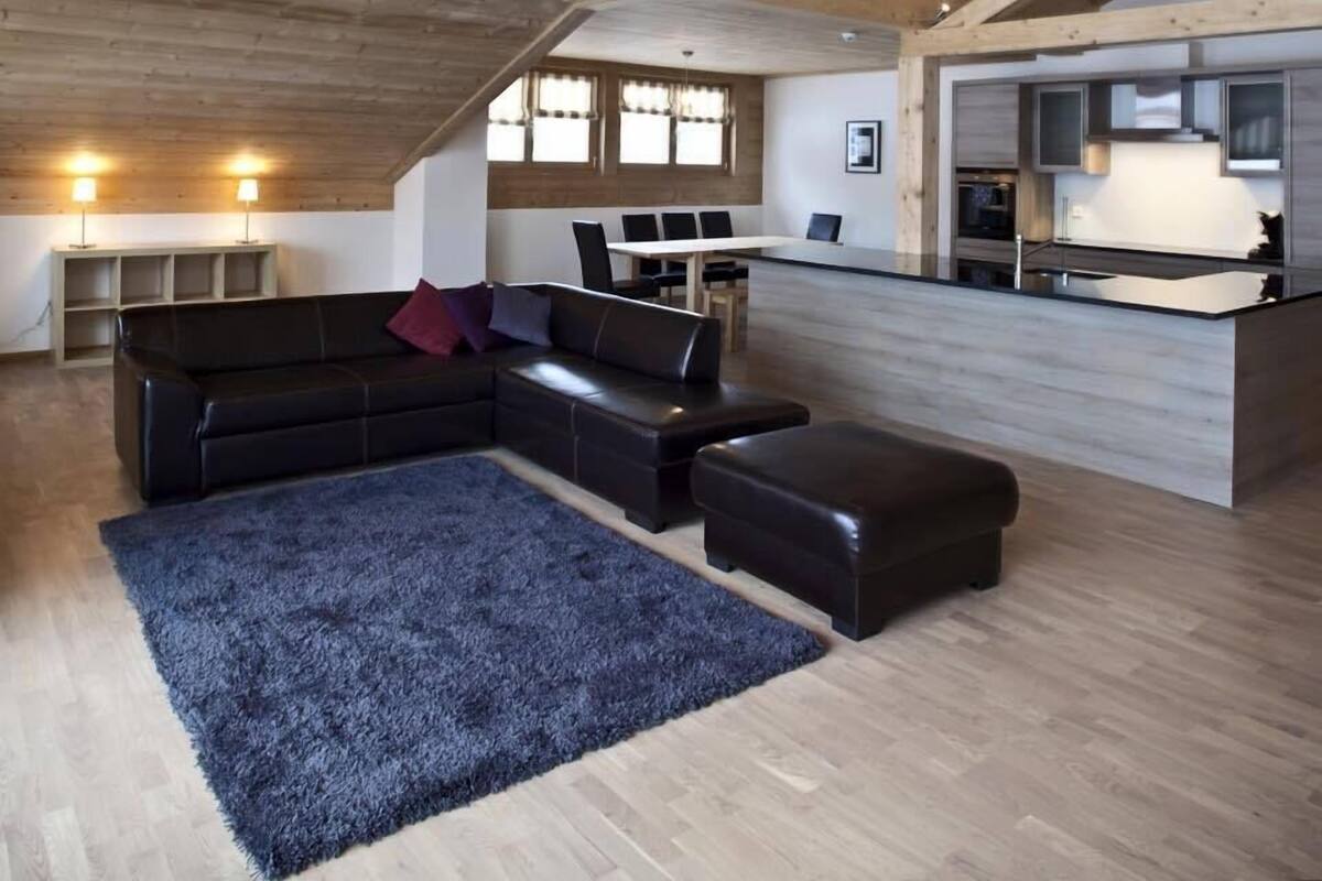Ein großzügiger Wohnbereich mit einer großen schwarzen Ledersofa, einem blauen Teppich und einer Holzboden.