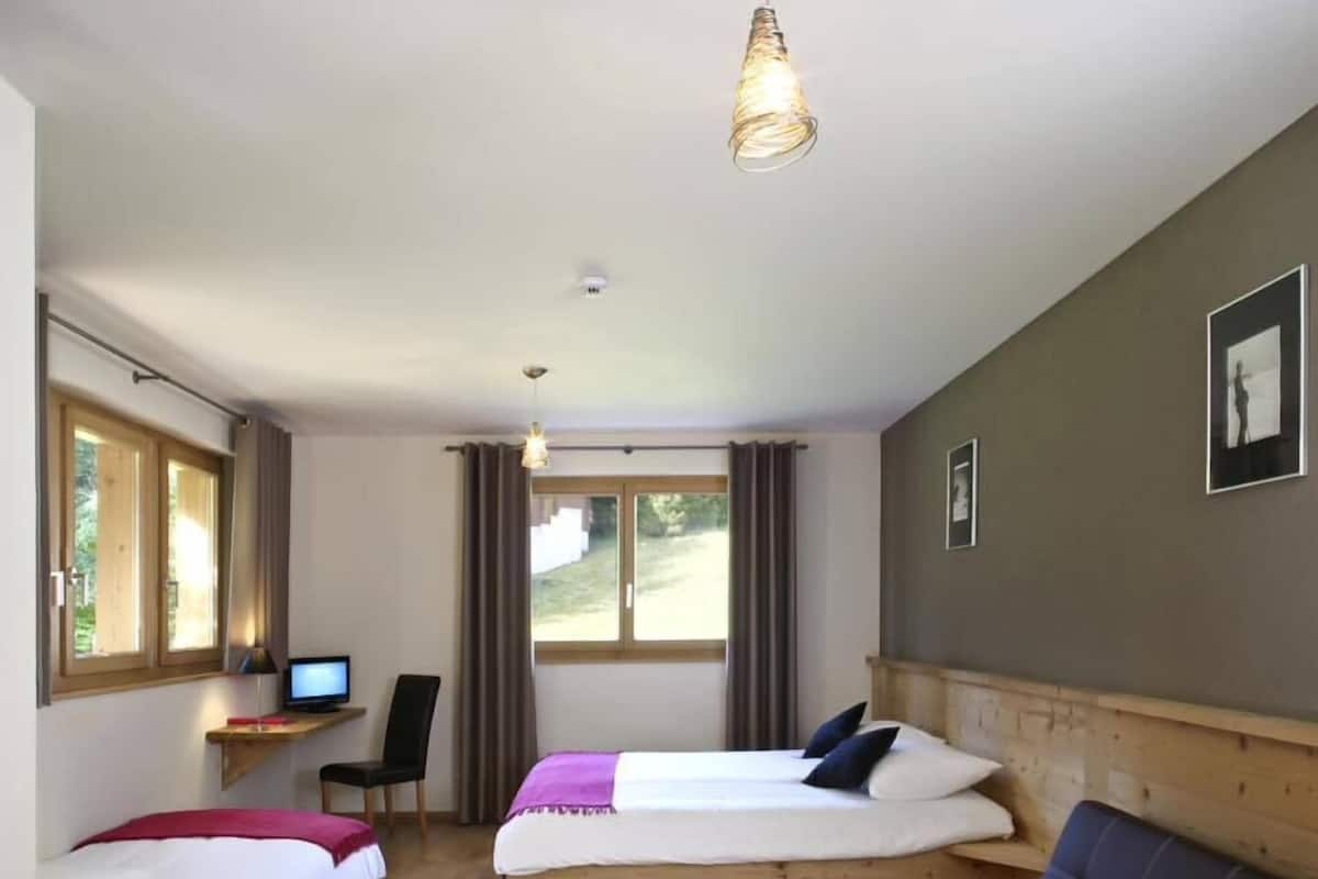 Ein Zimmer mit zwei Betten, einem Schreibtisch mit Computer, einer Couch und einer Hängelampe.