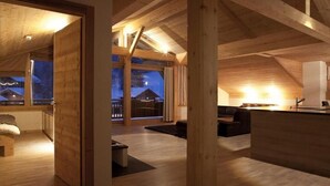A cozy, well-lit wooden interior with a large open space, a seating area, and a view of the outside.
