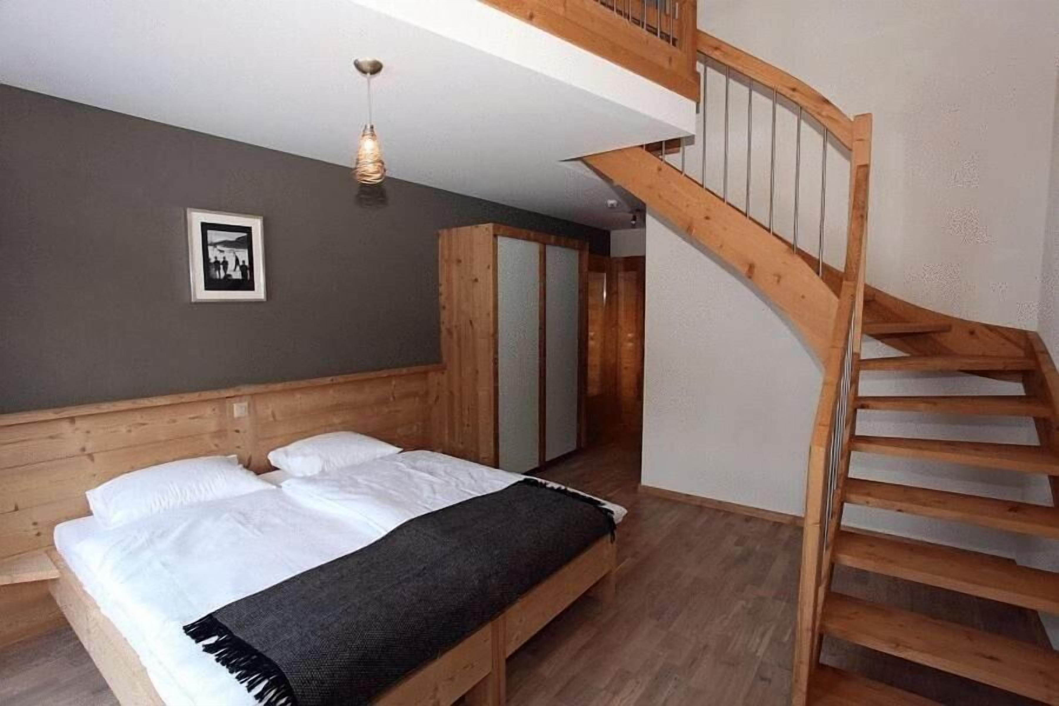 Une chambre à coucher avec un lit en bois, un escalier et un tableau encadré au mur.
