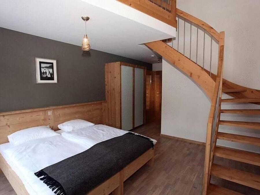 Une chambre à coucher avec un lit en bois, un escalier et un tableau encadré au mur.