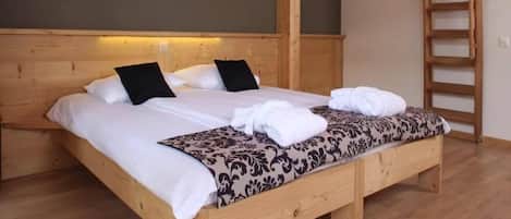 Una cama de madera con sábanas blancas y una colcha estampada, un cuadro en la pared y una escalera de madera apoyada contra la pared.