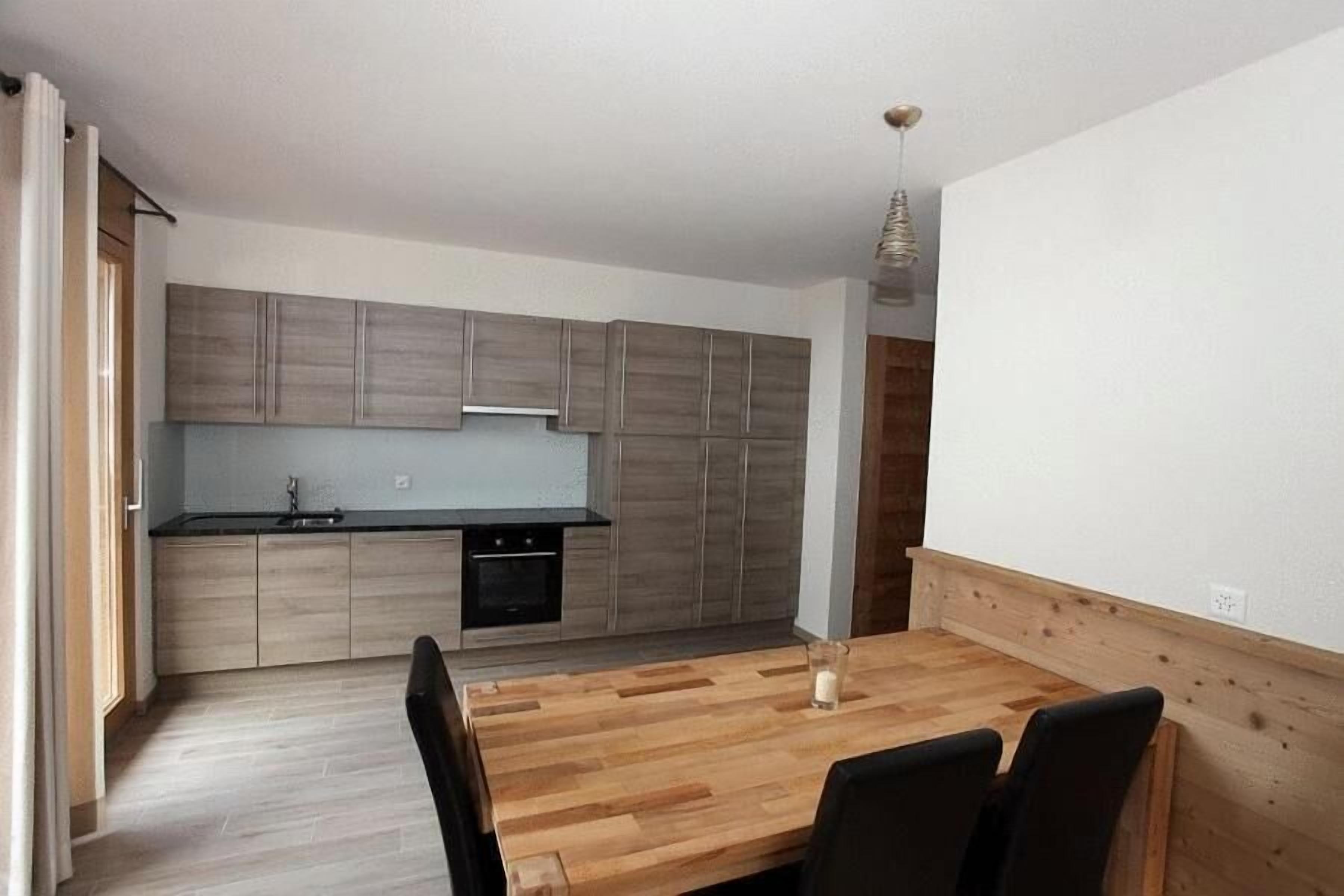 A modern kitchen with wooden cabinets and a central island, a dining table with chairs, and a pendant light.