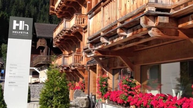 A wooden chalet with balconies, a sign for Helvetia, and potted plants.