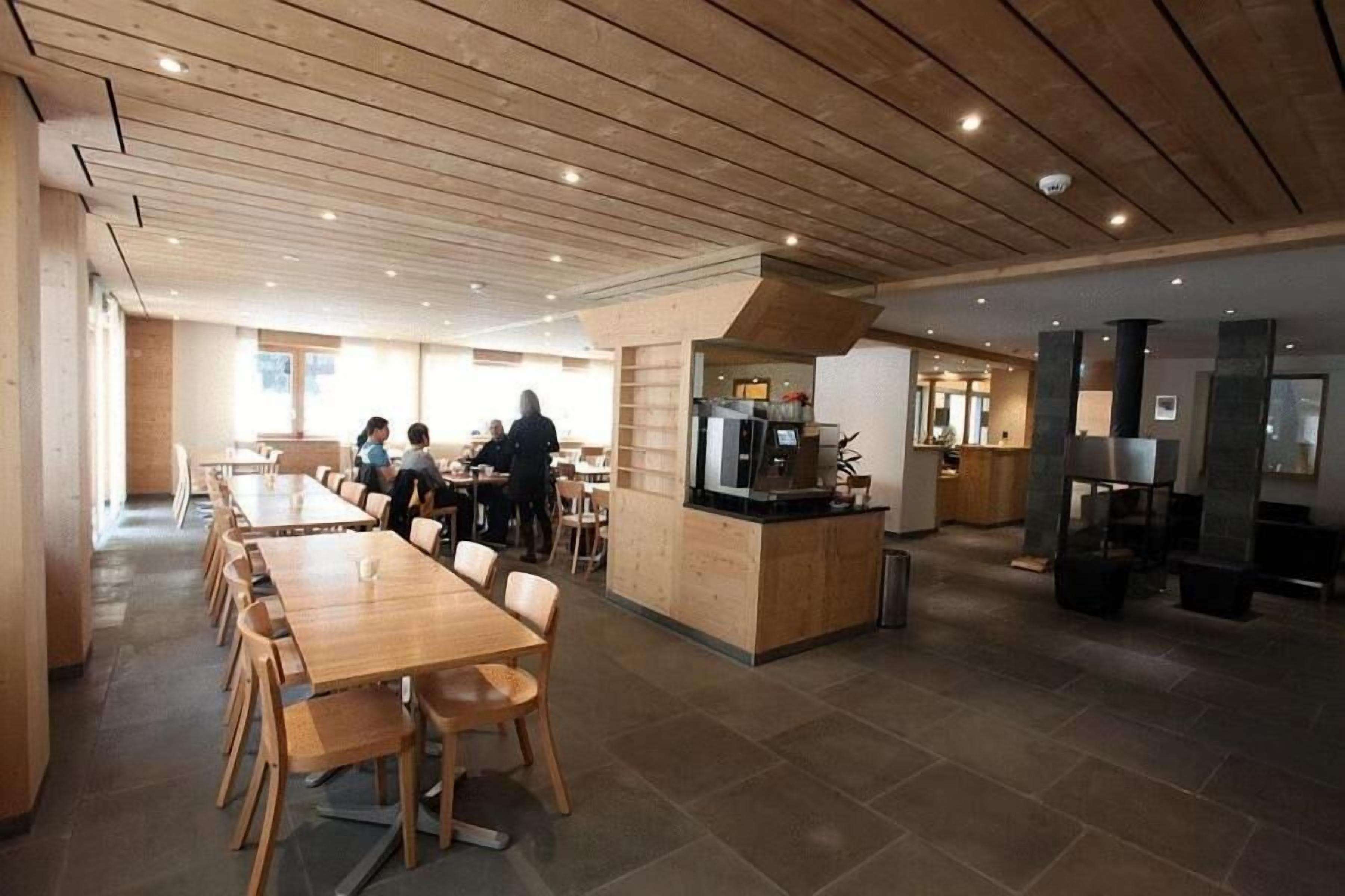 Un comedor amplio con mesas y sillas de madera, una barra central y una cocina al fondo.