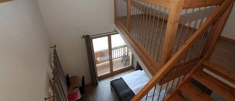 Habitación con techos altos, una escalera de madera, una cama y vistas al balcón exterior.