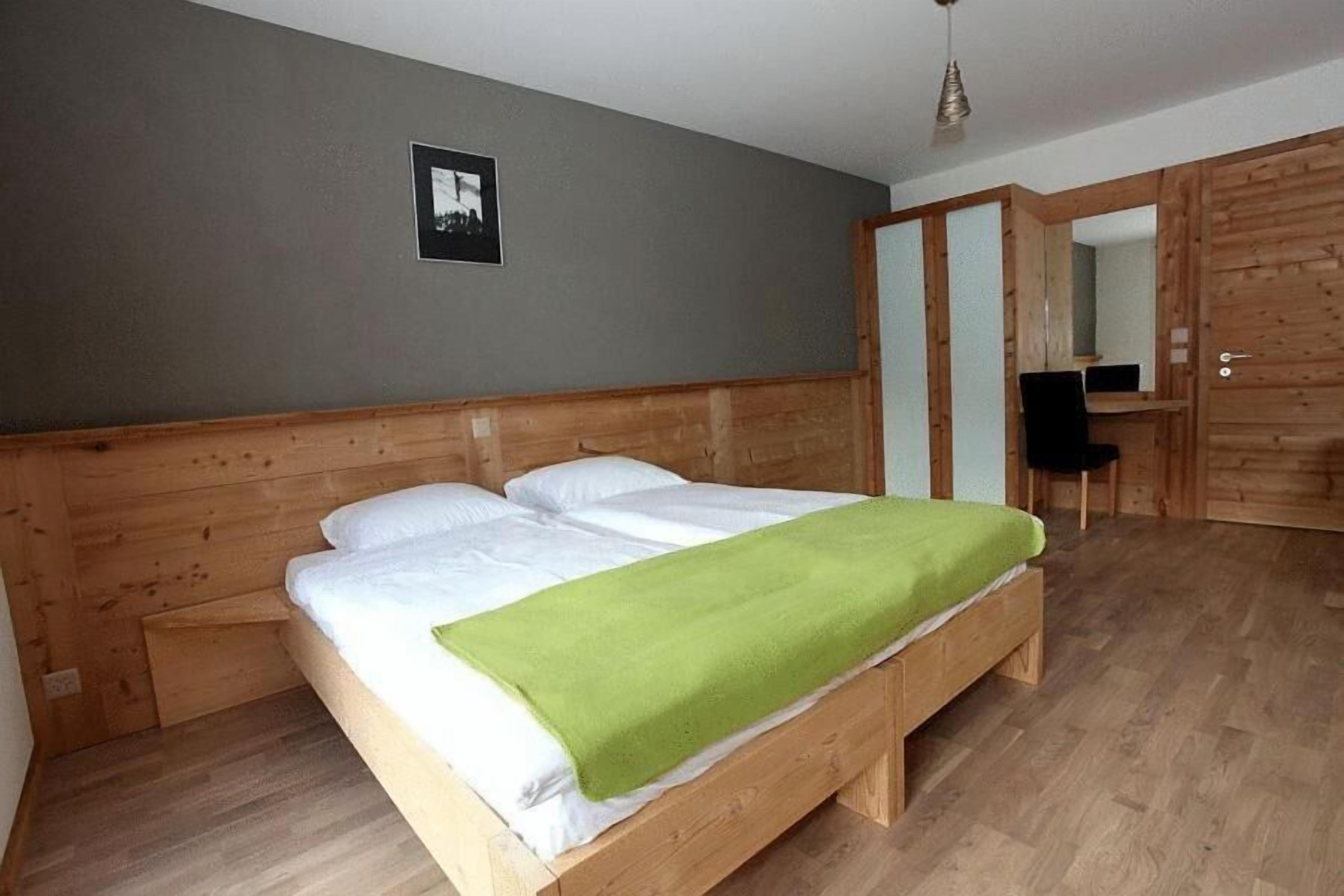 A wooden bed with white bedding and a green throw blanket in a room with wooden walls and floors.