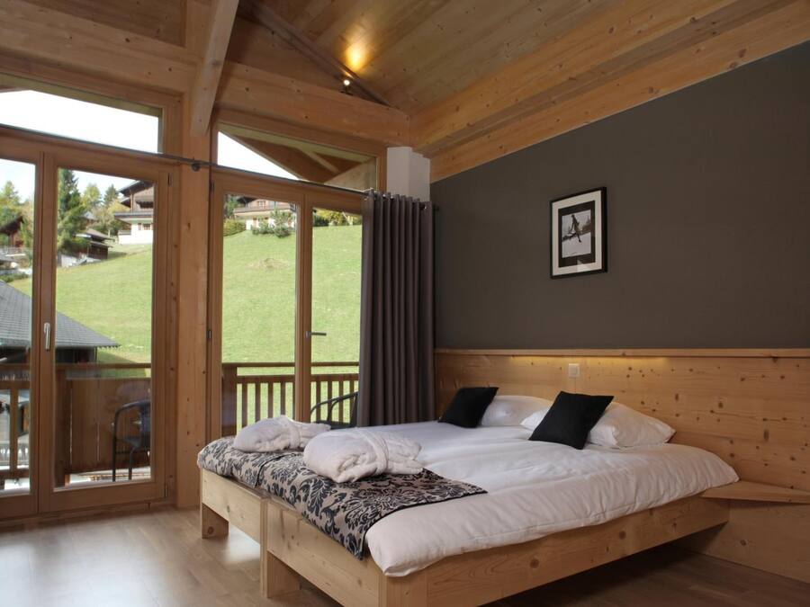 Une chambre avec un cadre en bois, dotée d’un grand lit, offrant une vue sur un espace verdoyant, et comprenant un coin repas avec une table et des chaises.