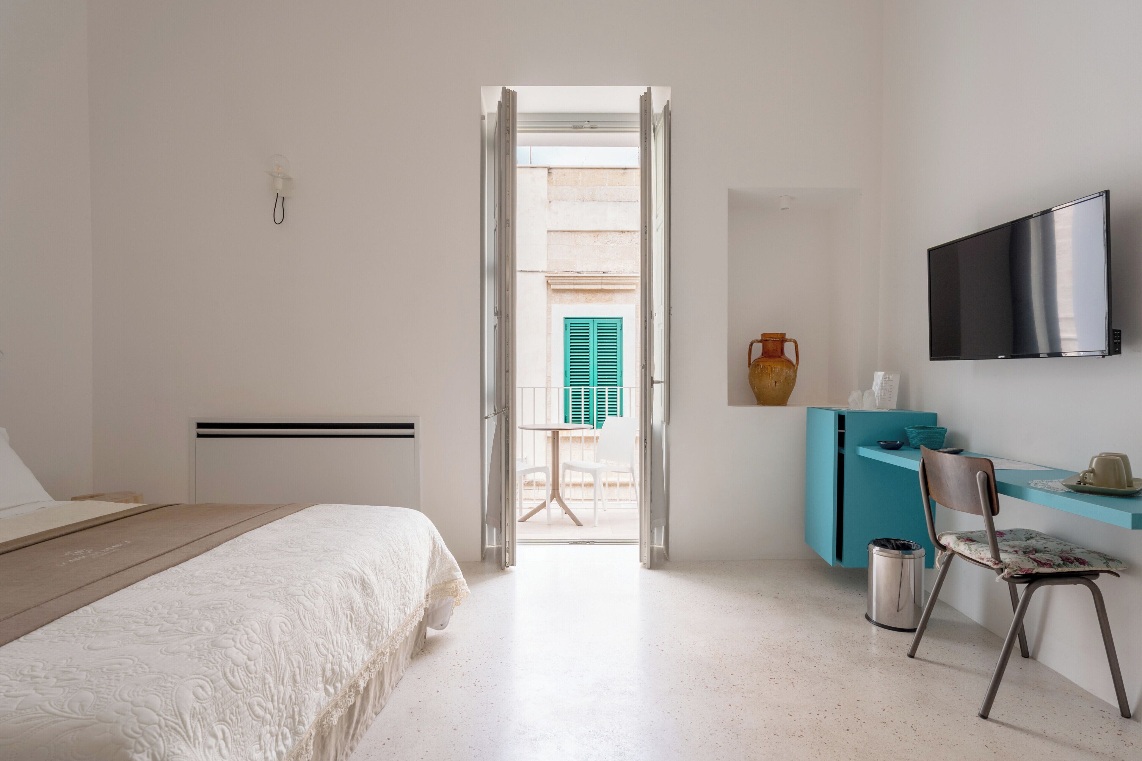 Un dormitorio con cama, escritorio, silla, televisor y una puerta abierta que da a un balcón.