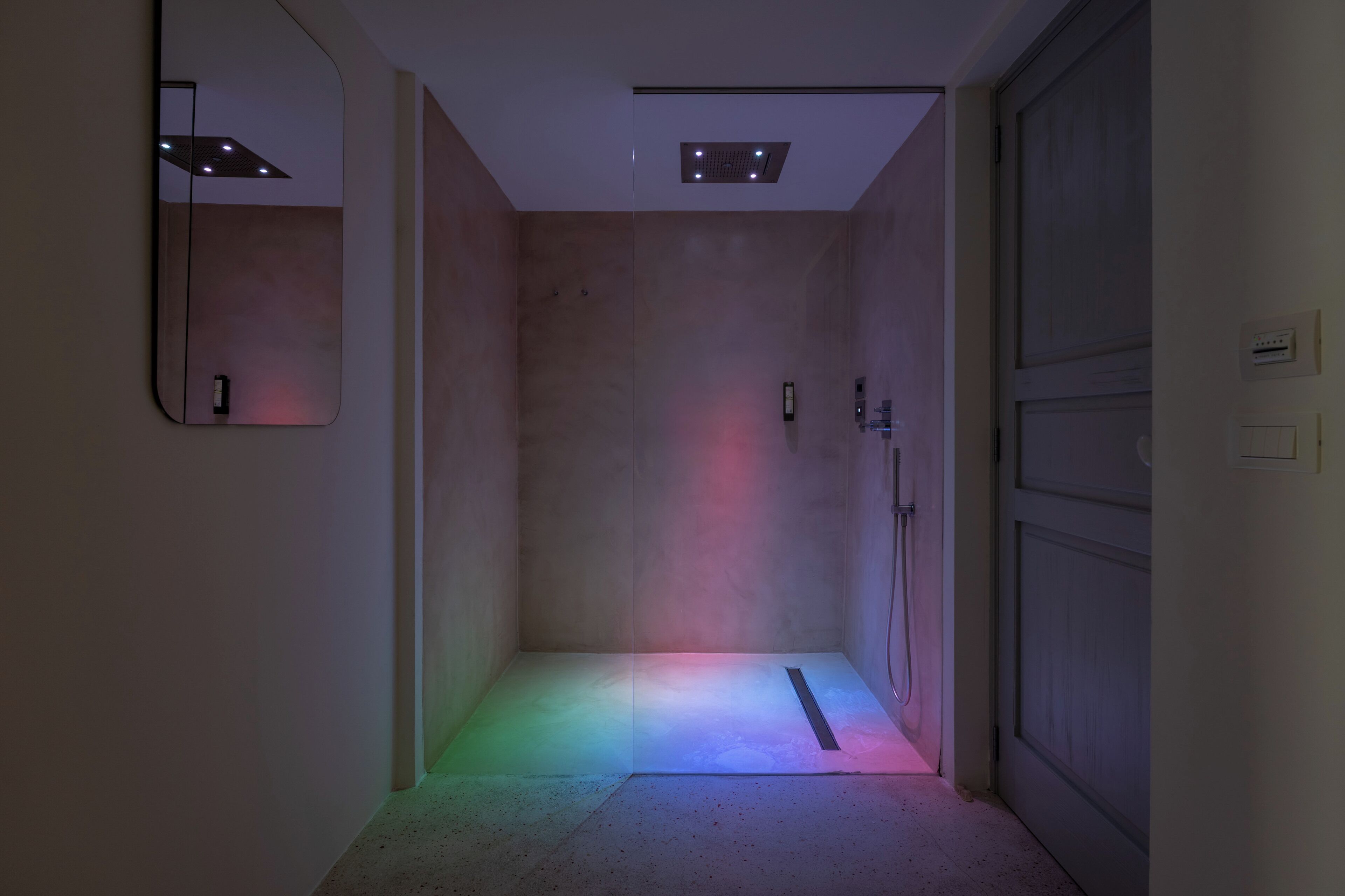 A narrow hallway with a shower area, a door on the right, and a mirror on the left.