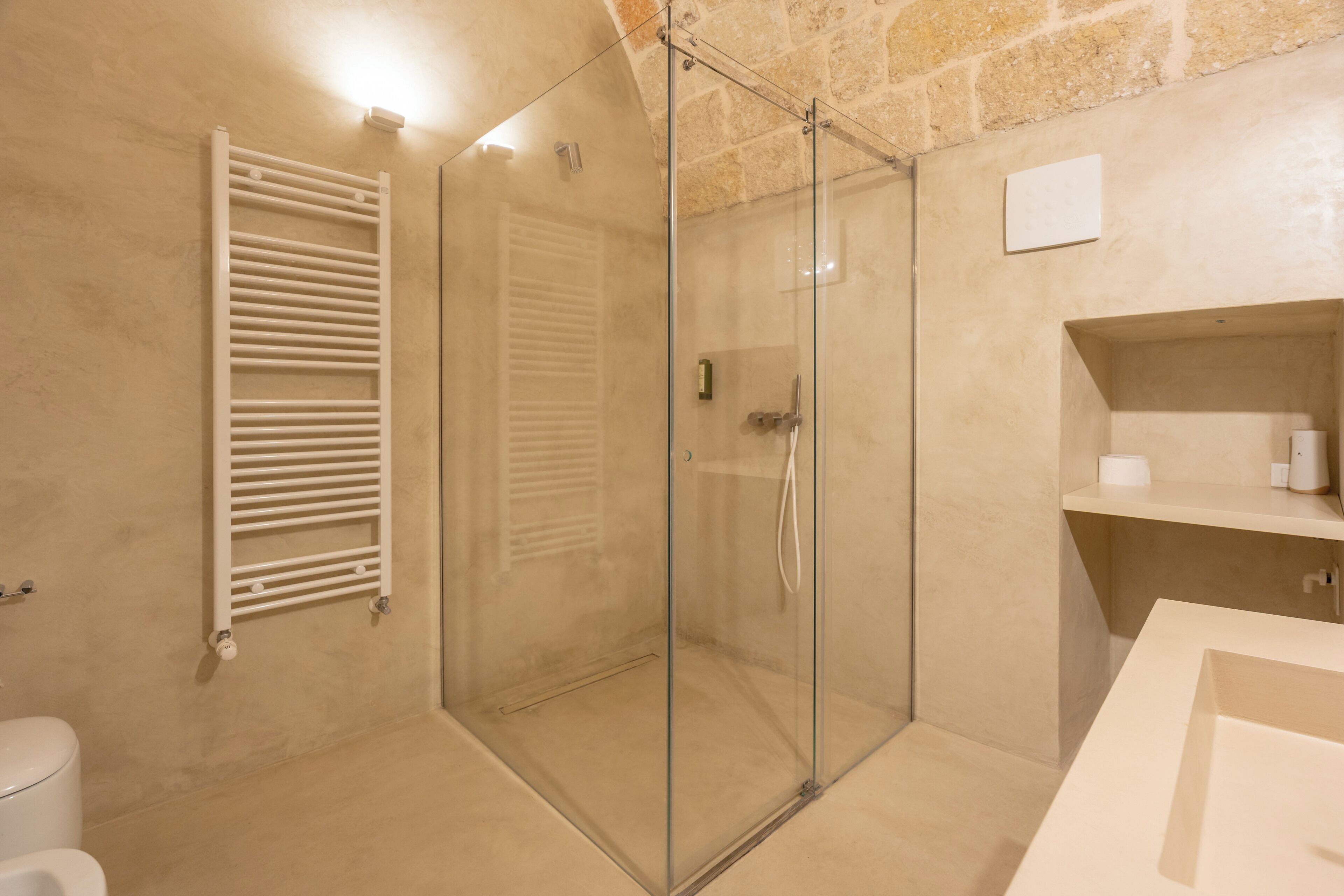 A modern bathroom with a glass-enclosed shower, a white towel rack, and a beige tiled wall.