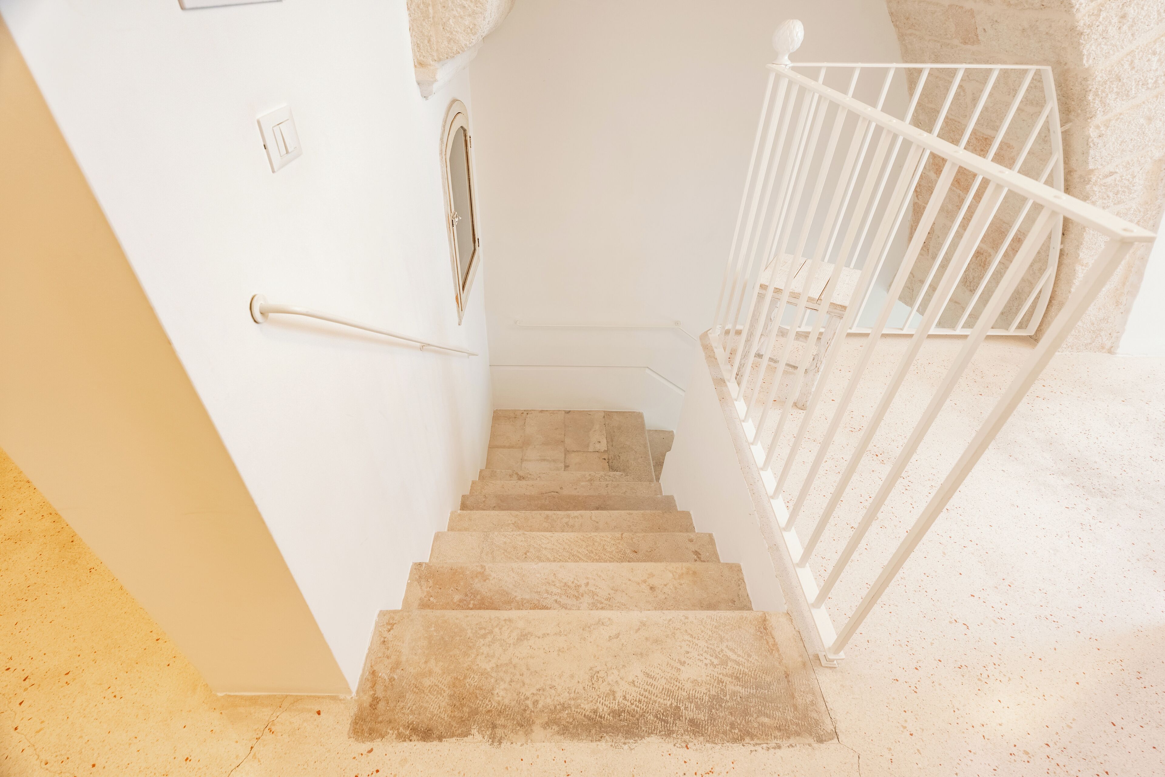 Eine Treppe mit Handlauf und weißer Brüstung, die zu einem Zwischenpodest mit einer Tür und einem kleinen Fenster führt.