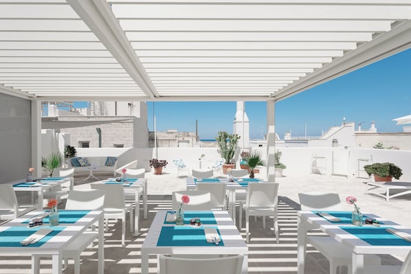 An outdoor dining area with white tables and chairs, blue placemats, and potted plants. - Donna Domenica Boutique Suites (Polignano a Mare)