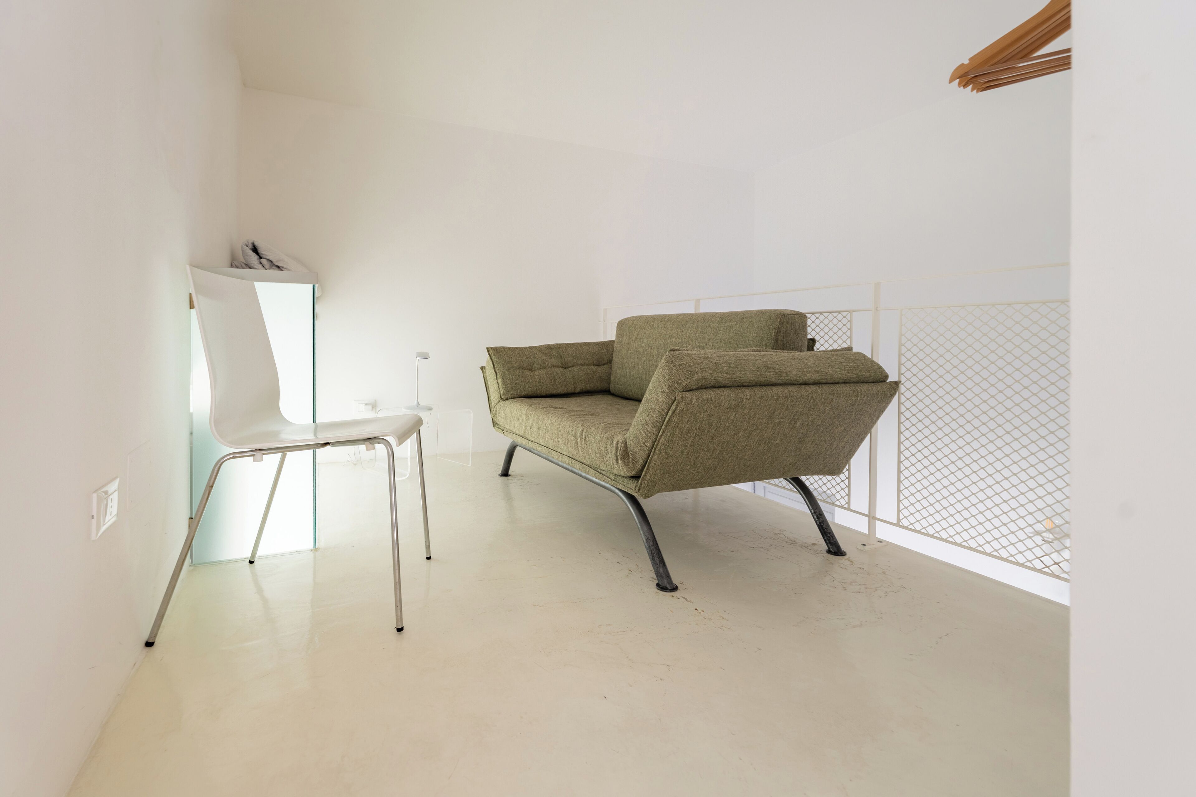 Une pièce au décor minimaliste, avec un fauteuil vert à revêtement en tissu, une chaise blanche et un sol blanc.