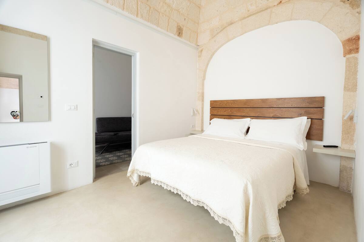 A bedroom with a white bed, a wooden headboard, and a stone wall.