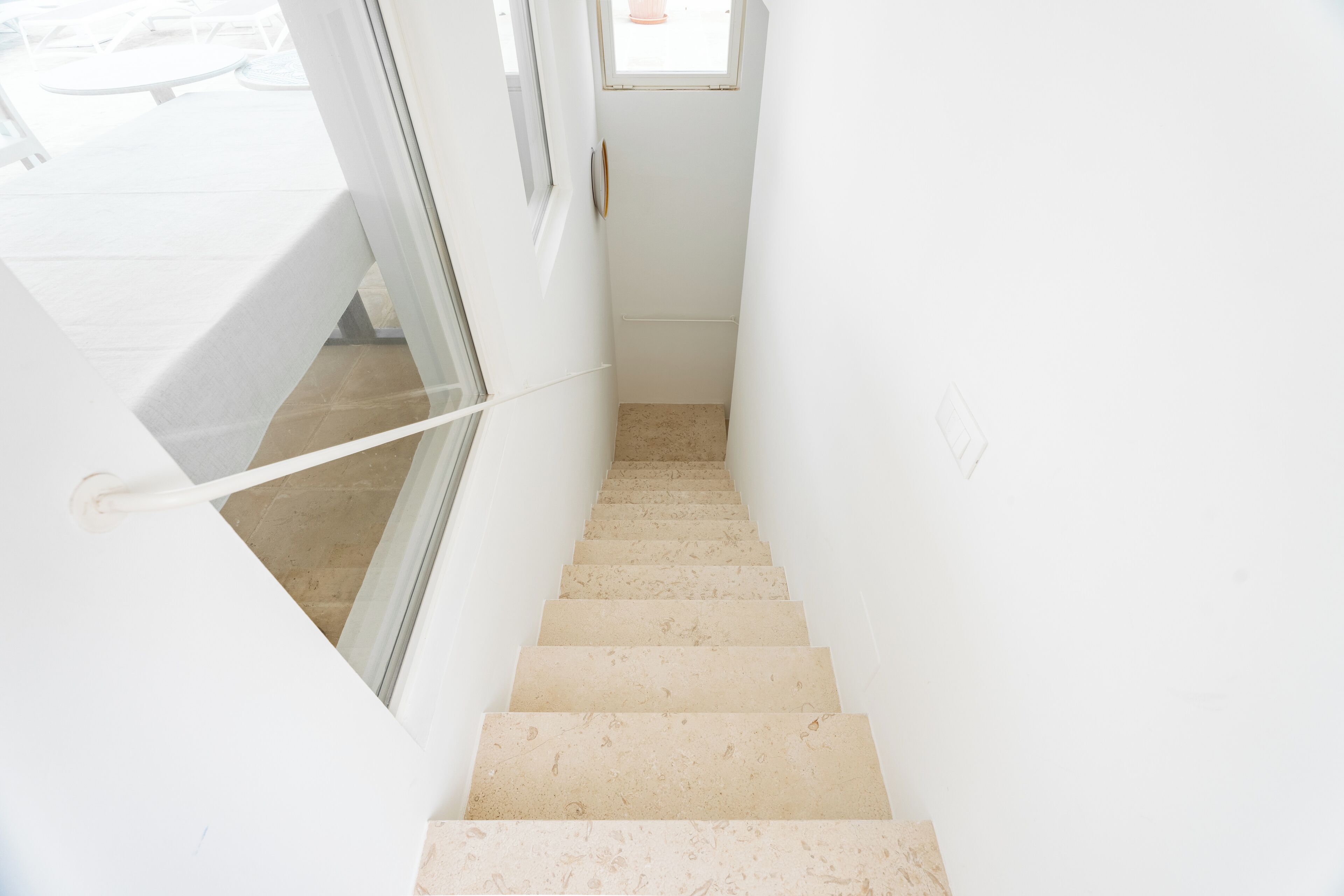 Un escalier étroit et blanc, doté d’une rampe, mène à une porte surmontée d’une fenêtre.
