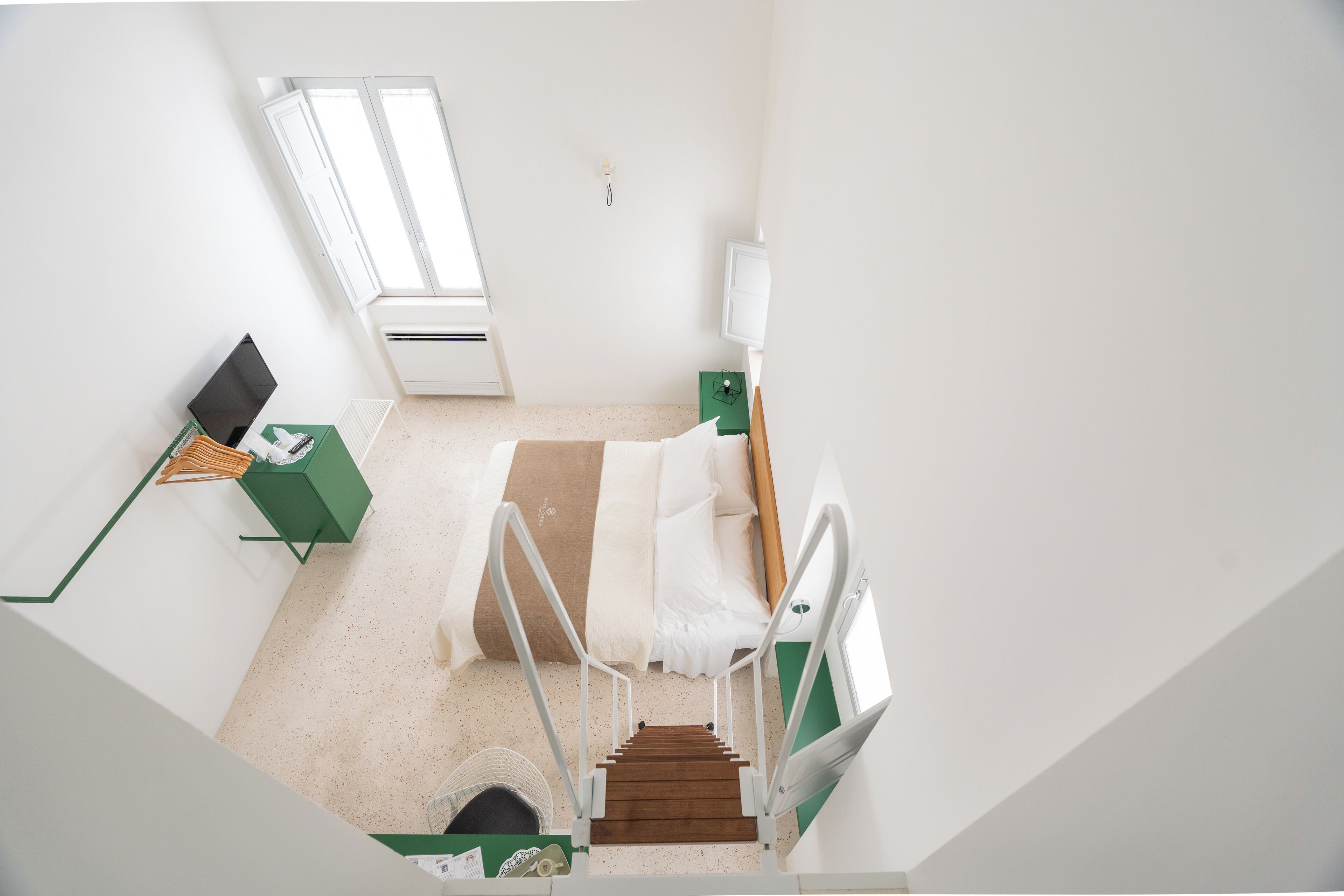 A bedroom with a bed, a desk, a chair, a window, and a staircase.