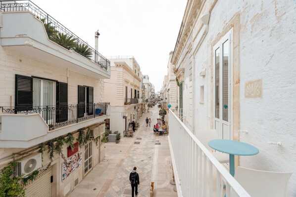 Una calle estrecha flanqueada por edificios con balcones y barandillas, y una persona caminando por la calle.