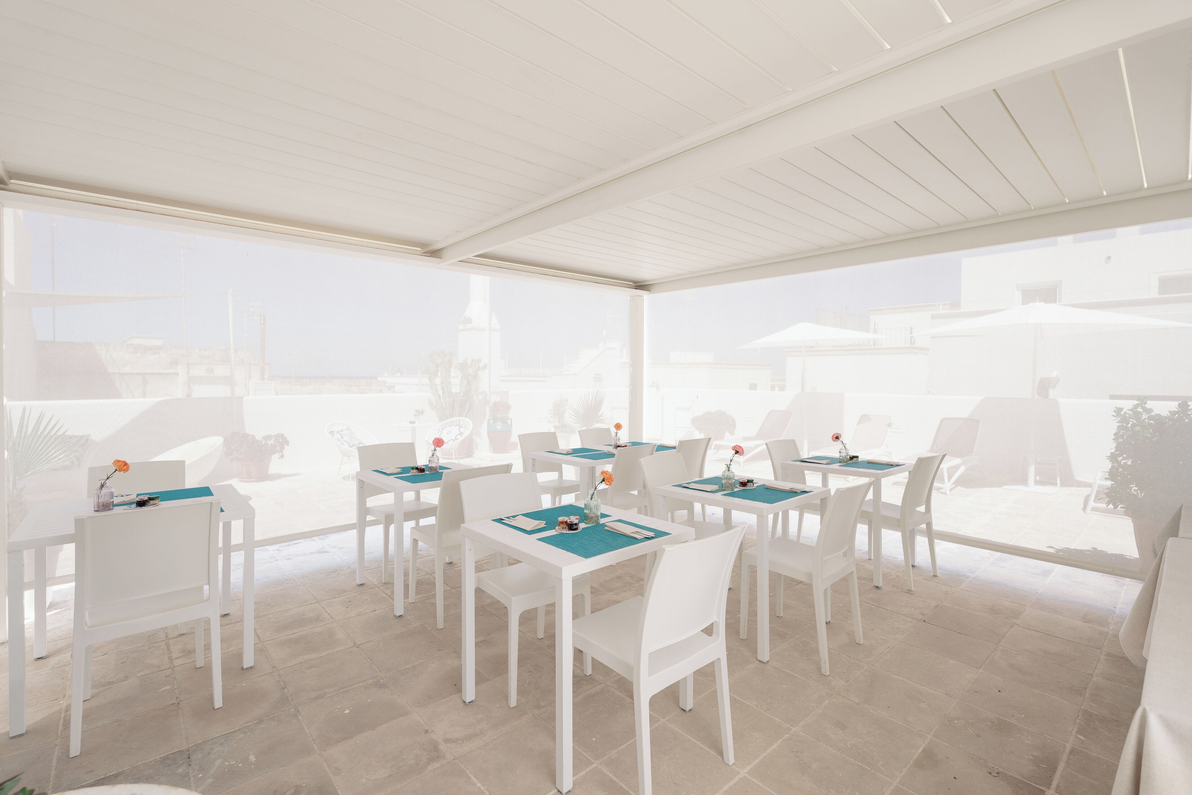Un patio al aire libre con mesas y sillas blancas, dispuesto en un espacio amplio.