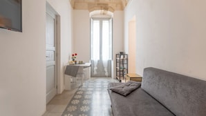 A narrow hallway with a grey sofa, a small table, and a chair. - Donna Domenica Boutique Suites (Polignano a Mare)
