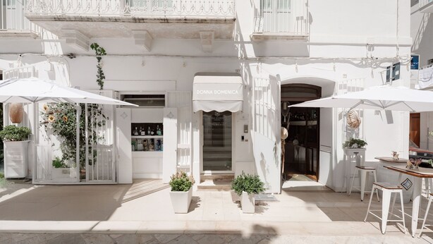 A white building with a storefront labeled "DONNA DOMENICA" and outdoor seating with umbrellas. - Donna Domenica Boutique Suites (Polignano a Mare)