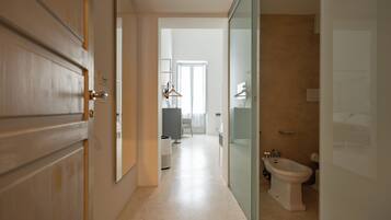 A hallway leading to a bathroom with a bidet, a mirror, and a door.