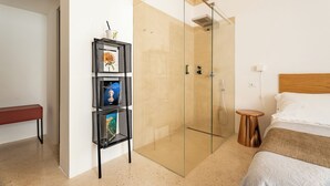 A modern hotel room with a glass-enclosed shower, a wooden headboard, a bedside table, and a shelf with decorative items. - Donna Domenica Boutique Suites (Polignano a Mare)