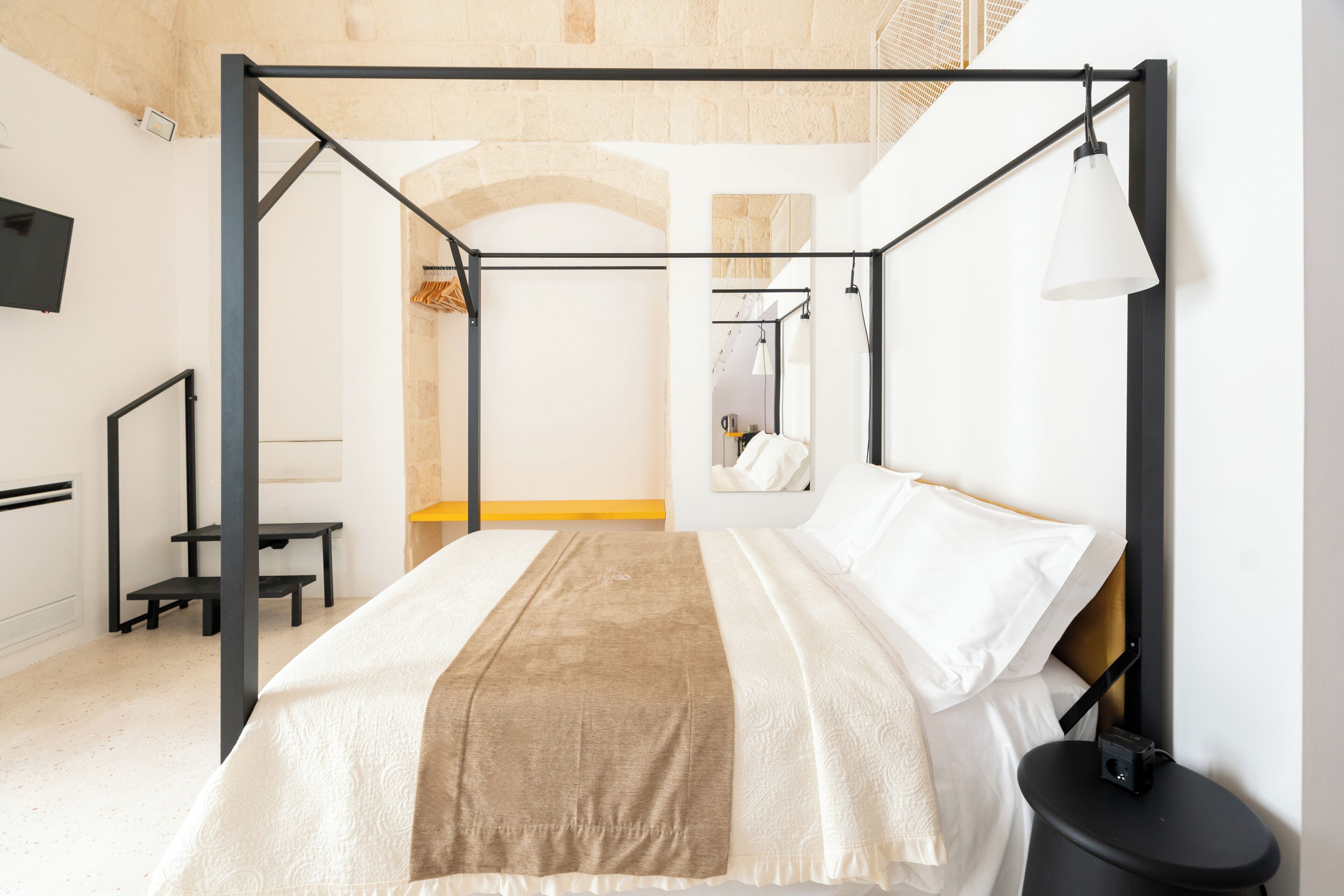 A modern bedroom with a four-poster bed, a bedside table, and a hanging lamp.