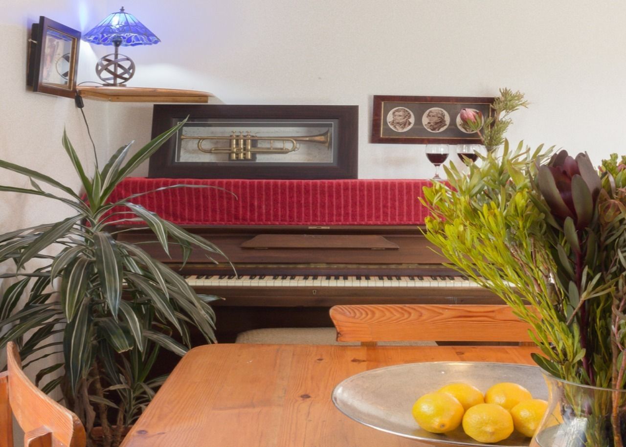 Una habitación con un piano, una mesa con un cuenco de cristal lleno de limones y una planta en maceta.